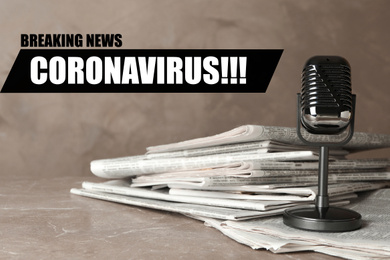 Image of Word CORONAVIRUS, newspapers and vintage microphone on marble table. Journalist's work