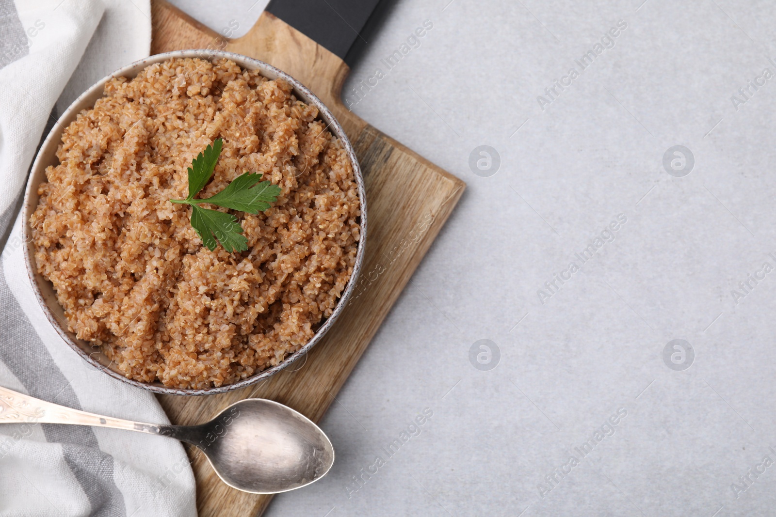 Photo of Tasty wheat porridge with parsley in bowl and spoon on light table, top view. Space for text