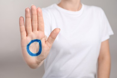 Photo of Woman showing blue circle drawn on palm against light grey background, closeup. World Diabetes Day