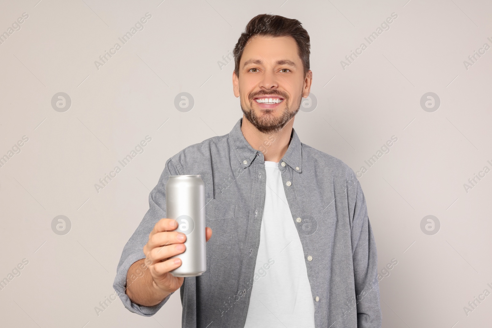 Photo of Happy man holding tin can with beverage on light grey background