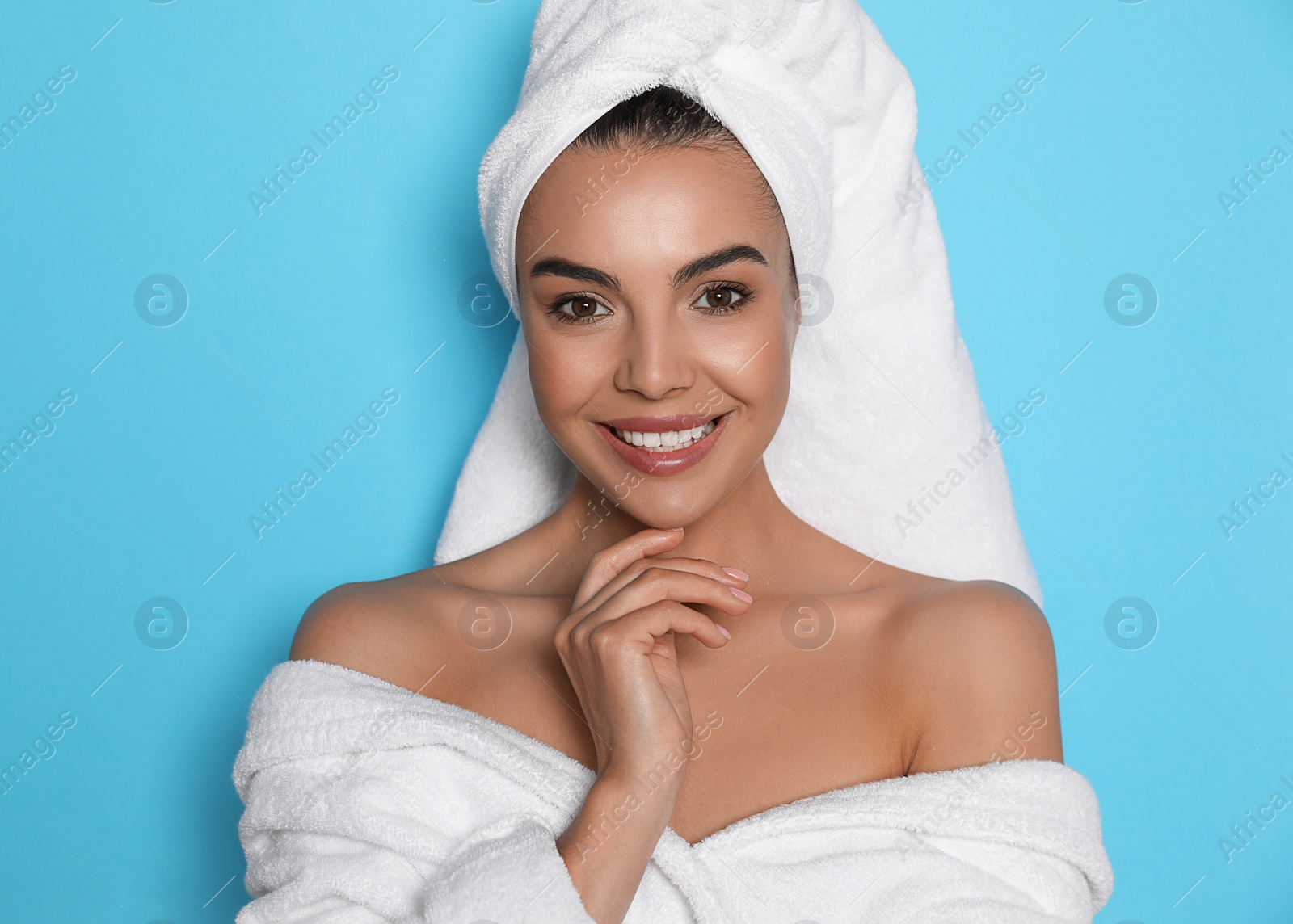 Photo of Beautiful young woman wearing bathrobe and towel on head against light blue background