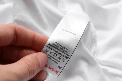 Woman holding clothing label on white garment, closeup