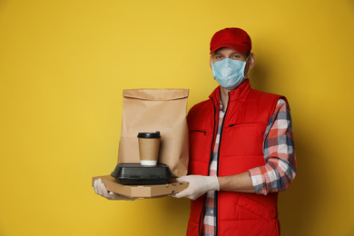 Courier in protective mask and gloves holding order on yellow background. Food delivery service during coronavirus quarantine