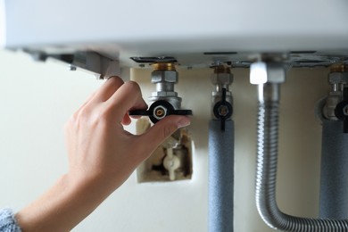 Photo of Woman turning on valve of gas boiler, closeup