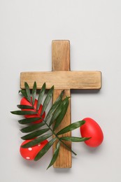 Wooden cross, painted Easter eggs and palm leaf on light grey background, flat lay