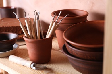 Set of different crafting tools and clay dishes on wooden table in workshop