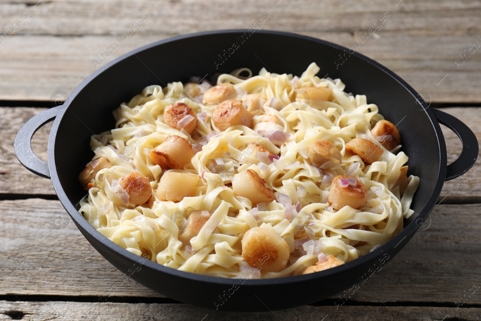 Photo of Delicious scallop pasta with onion in pan on wooden table, closeup