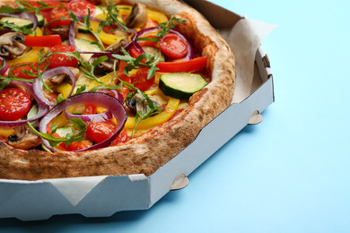 Photo of Delicious hot vegetable pizza in cardboard box on light blue background, closeup