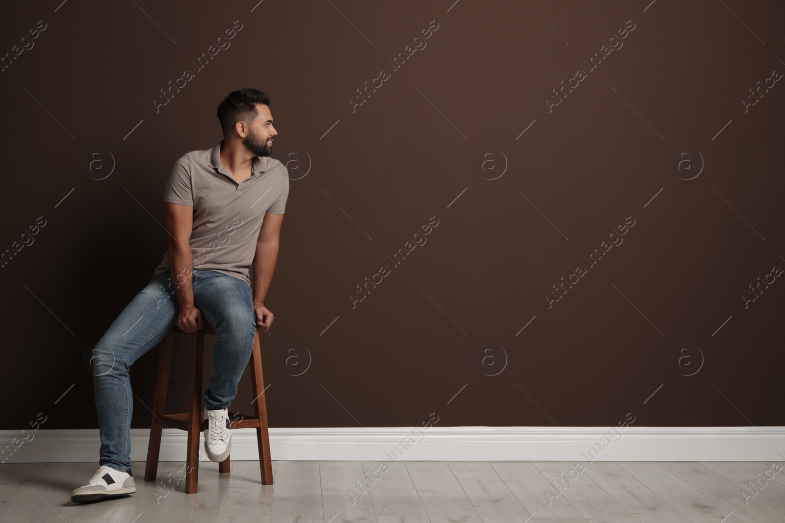 Photo of Handsome young man sitting on stool near brown wall. Space for text