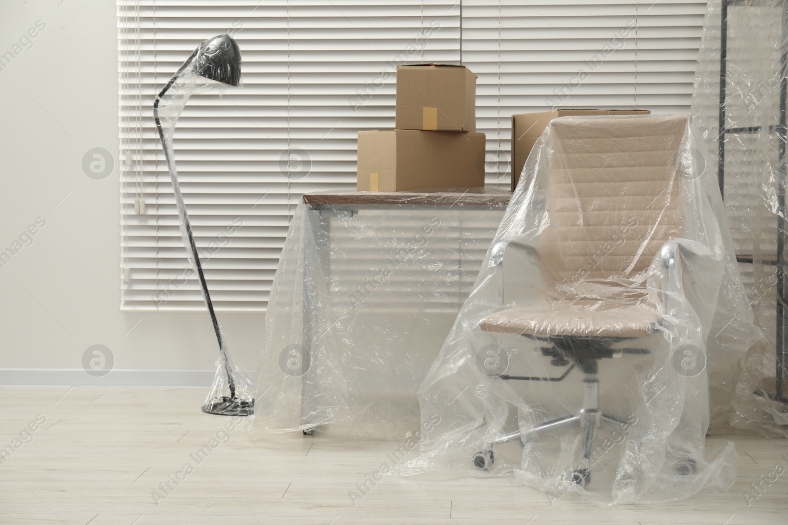 Photo of Modern furniture covered with plastic film and boxes at home