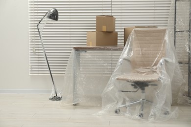 Photo of Modern furniture covered with plastic film and boxes at home