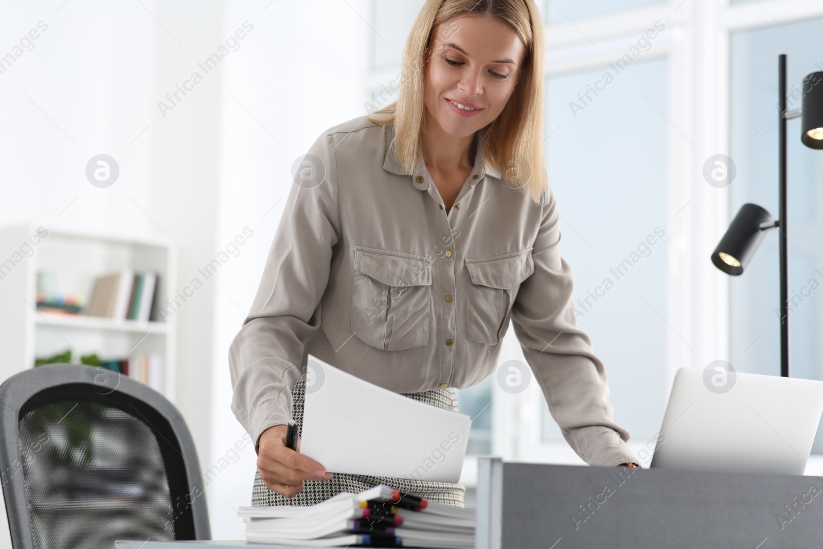 Photo of Happy woman working with documents at table in modern office