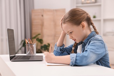 Photo of Little girl suffering from headache while doing homework at home