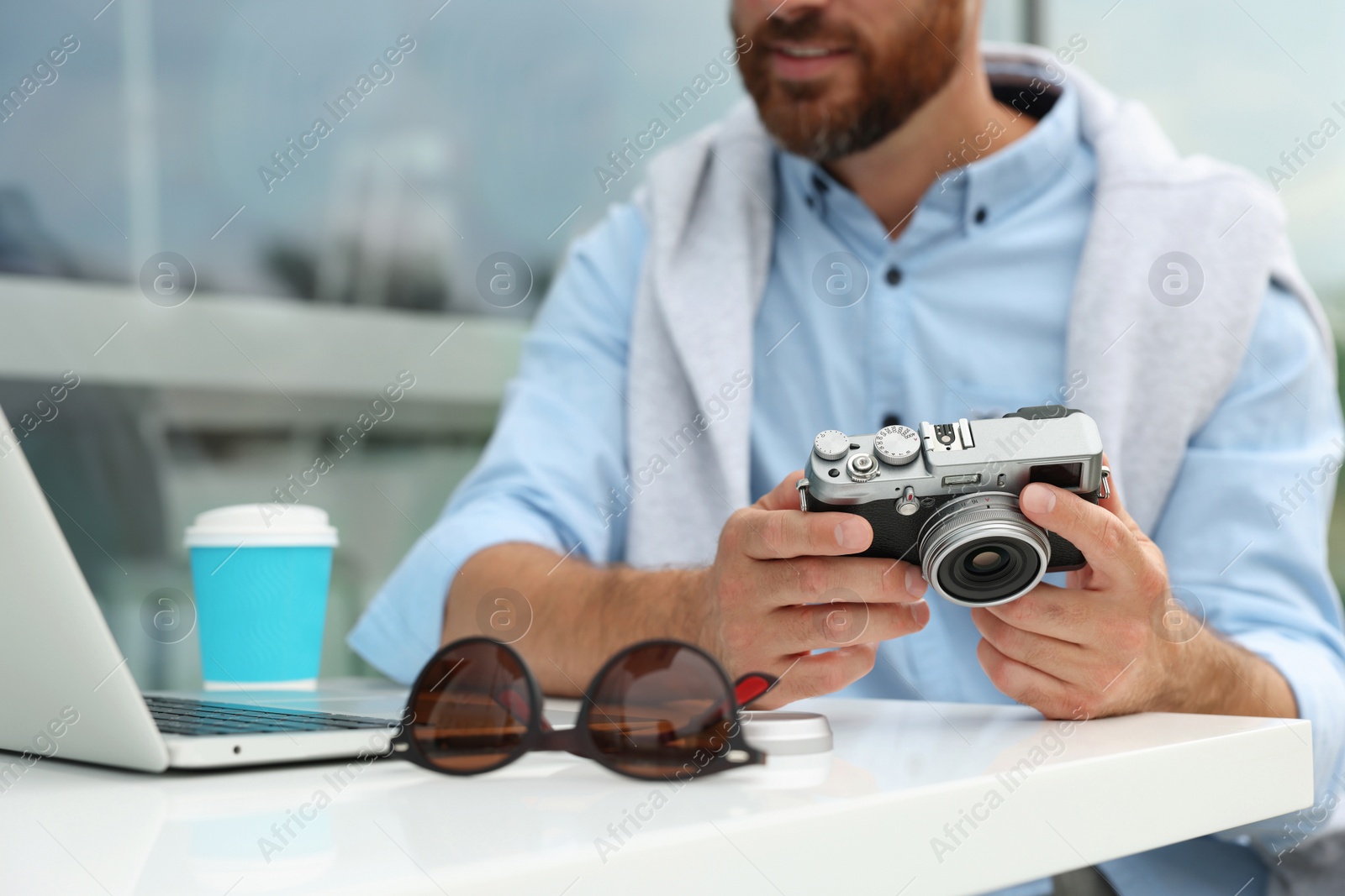Photo of Man with camera, coffee and laptop in outdoor cafe, closeup. Interesting hobby