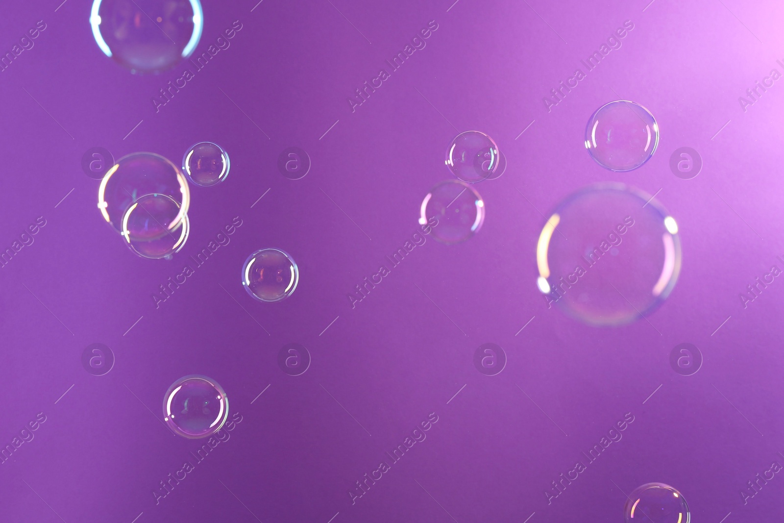 Photo of Beautiful transparent soap bubbles on violet background