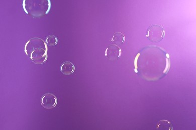 Photo of Beautiful transparent soap bubbles on violet background