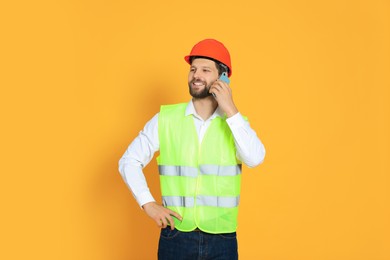 Photo of Man in reflective uniform talking on smartphone against orange background