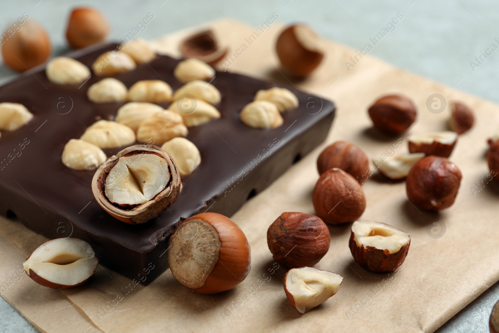 Photo of Delicious chocolate bar and hazelnuts on parchment paper, closeup