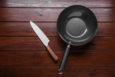 Photo of Empty iron wok and knife on wooden table, flat lay