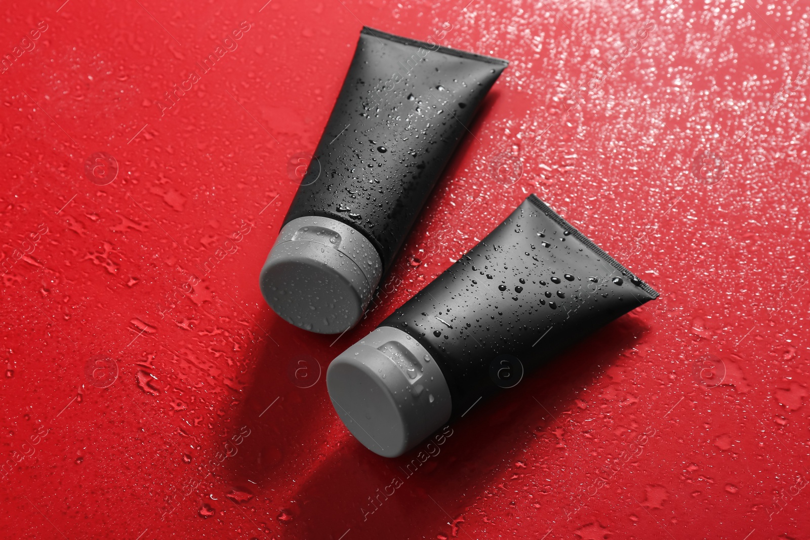 Photo of Black tubes on wet color surface, space for design. Men's cosmetic products