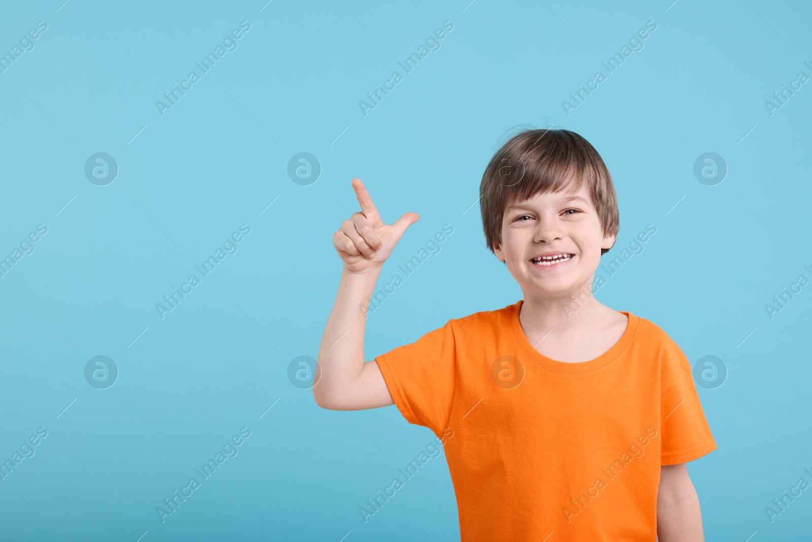 Photo of Cute little boy pointing at something on light blue background, space for text