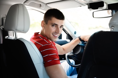 Photo of Attractive young man driving luxury car, view from backseat