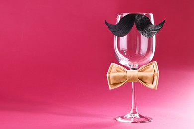 Photo of Man's face made of artificial mustache, bow tie and wine glass on crimson background. Space for text