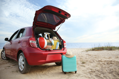 Photo of Red car luggage on beach, space for text. Summer vacation trip