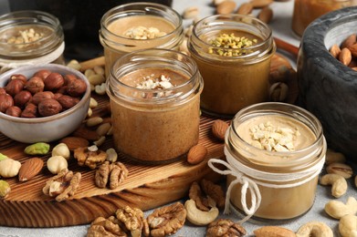 Photo of Tasty nut butters in jars and raw nuts on light grey table