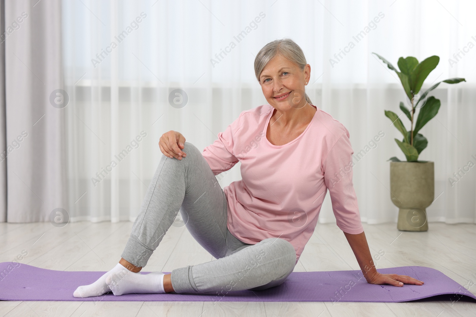 Photo of Happy senior woman sitting on mat at home. Yoga practice