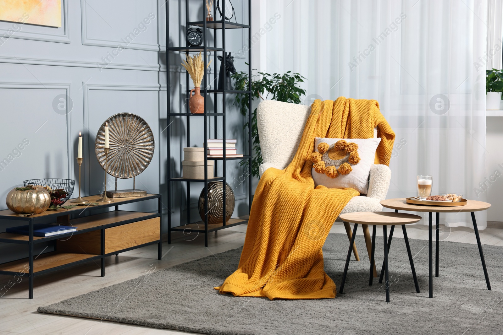 Photo of Stylish room interior with comfortable armchair, blanket and nesting tables