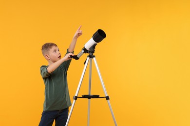 Photo of Surprised little boy with telescope pointing at something on orange background, space for text