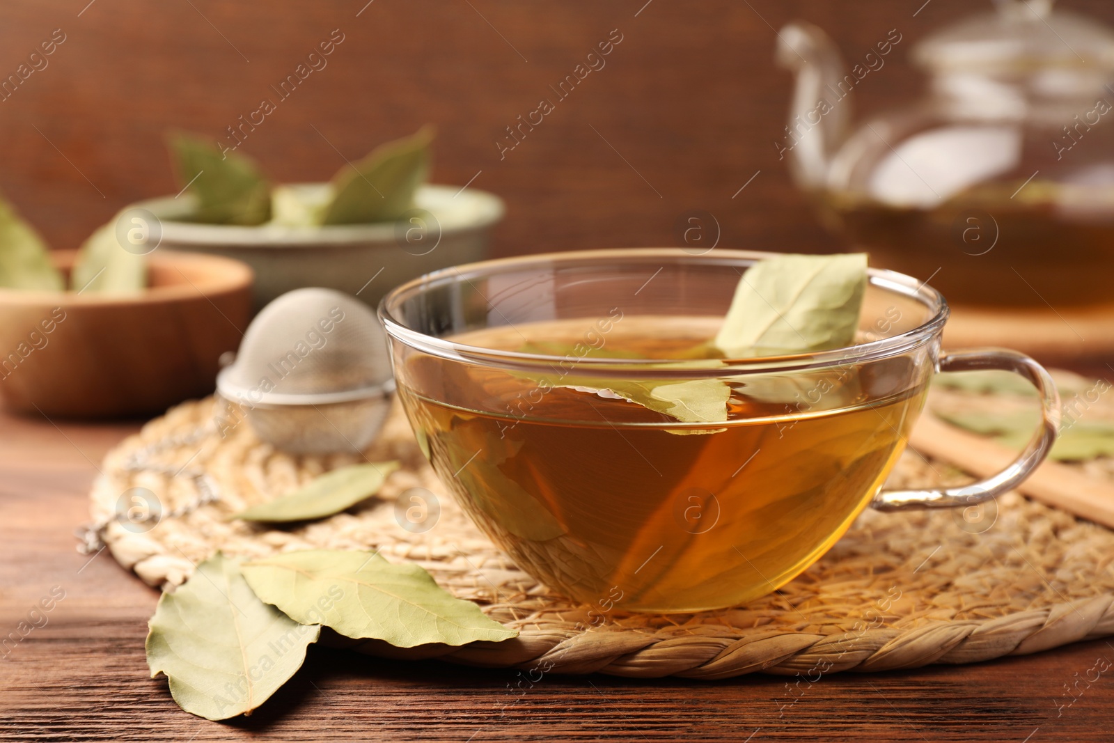 Photo of Cup of freshly brewed tea with bay leaves on wooden table, closeup