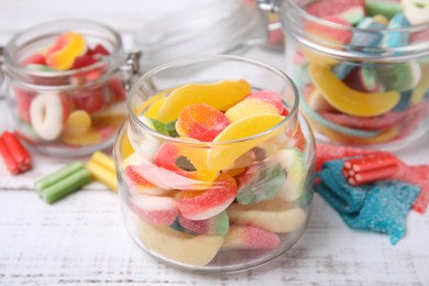 Photo of Tasty jelly candies in different jars on white wooden table, closeup