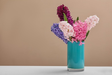 Photo of Beautiful hyacinths in blue vase on table against color background, space for text. Spring flowers