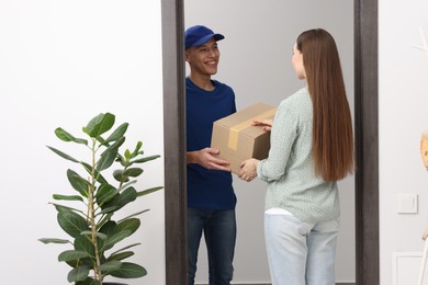 Happy courier giving parcel to receiver indoors