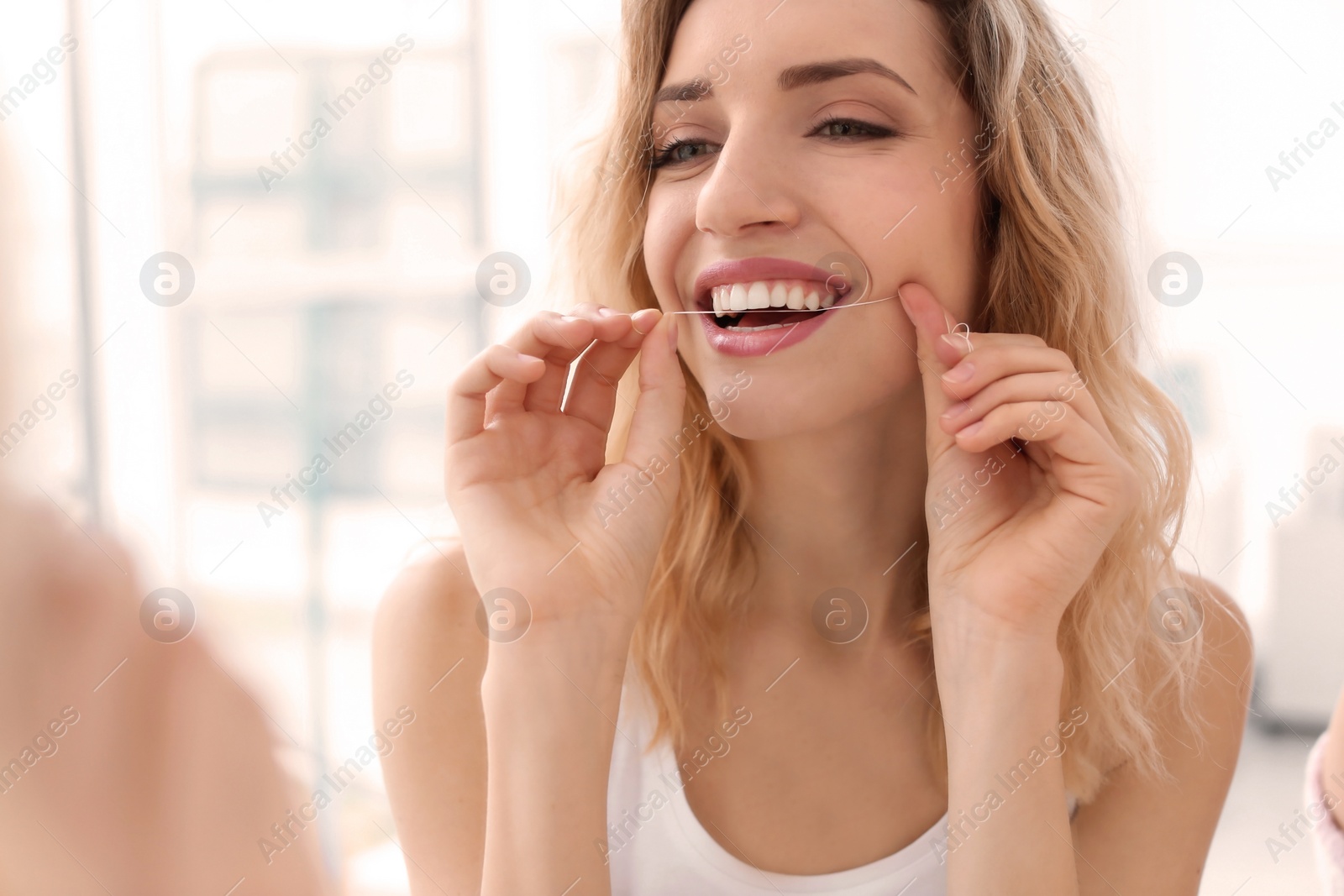 Photo of Young woman flossing her teeth indoors