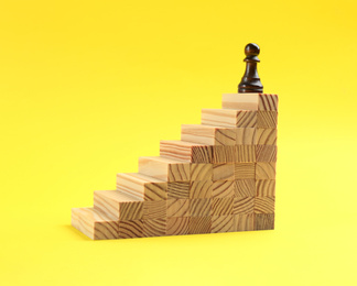 Pawn on top of stairs on yellow background. Career promotion concept