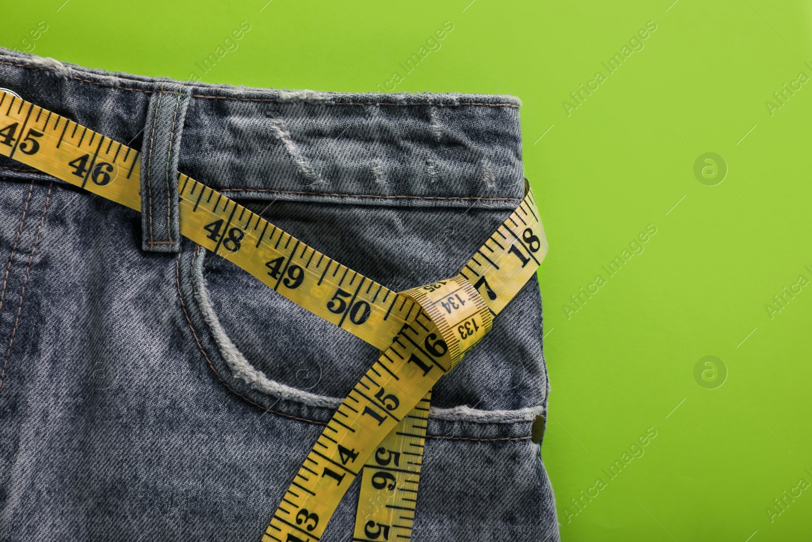 Photo of Jeans with measuring tape on green background, top view. Weight loss concept