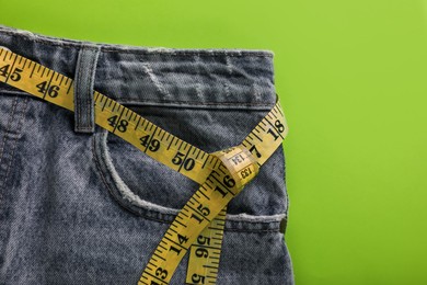 Photo of Jeans with measuring tape on green background, top view. Weight loss concept