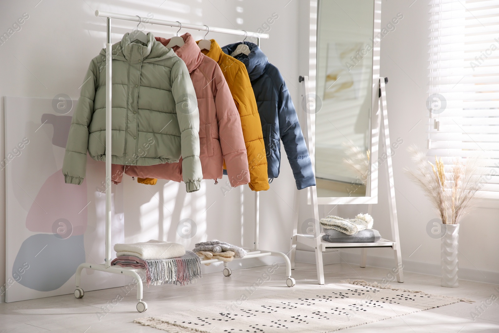 Photo of Different warm jackets on rack in stylish room interior