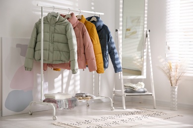 Photo of Different warm jackets on rack in stylish room interior