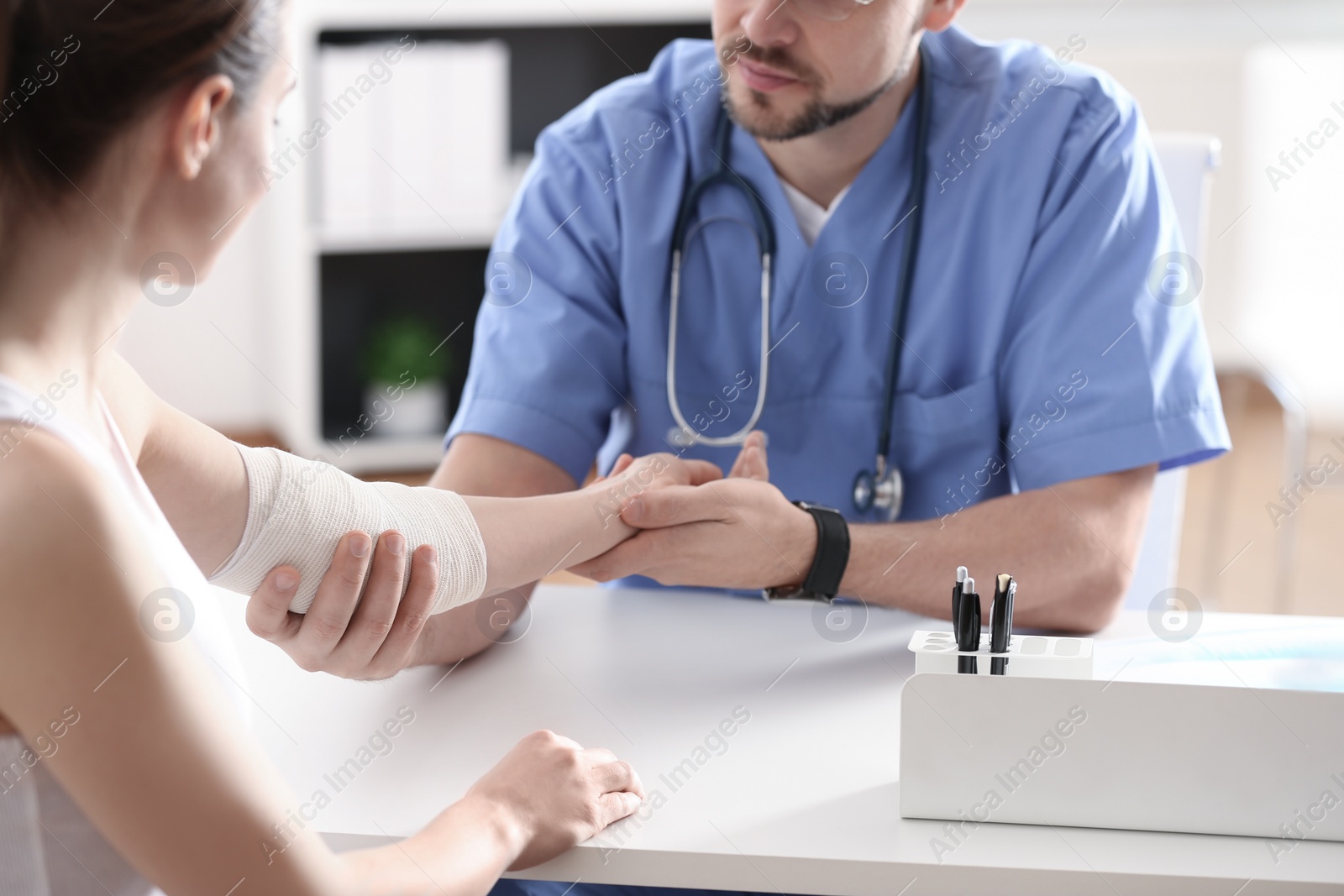 Photo of Male orthopedist applying bandage onto patient's elbow at table, closeup