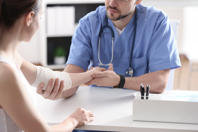 Photo of Male orthopedist applying bandage onto patient's elbow at table, closeup