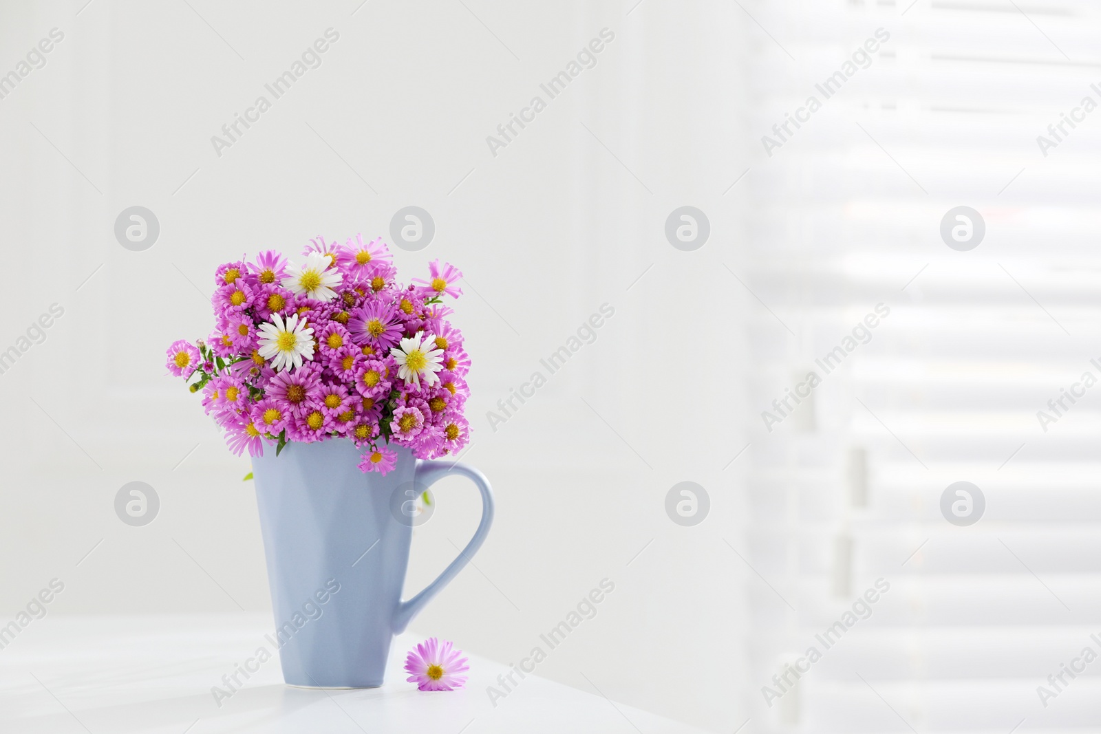 Photo of Cup with beautiful flowers on white table in light room. Space for text