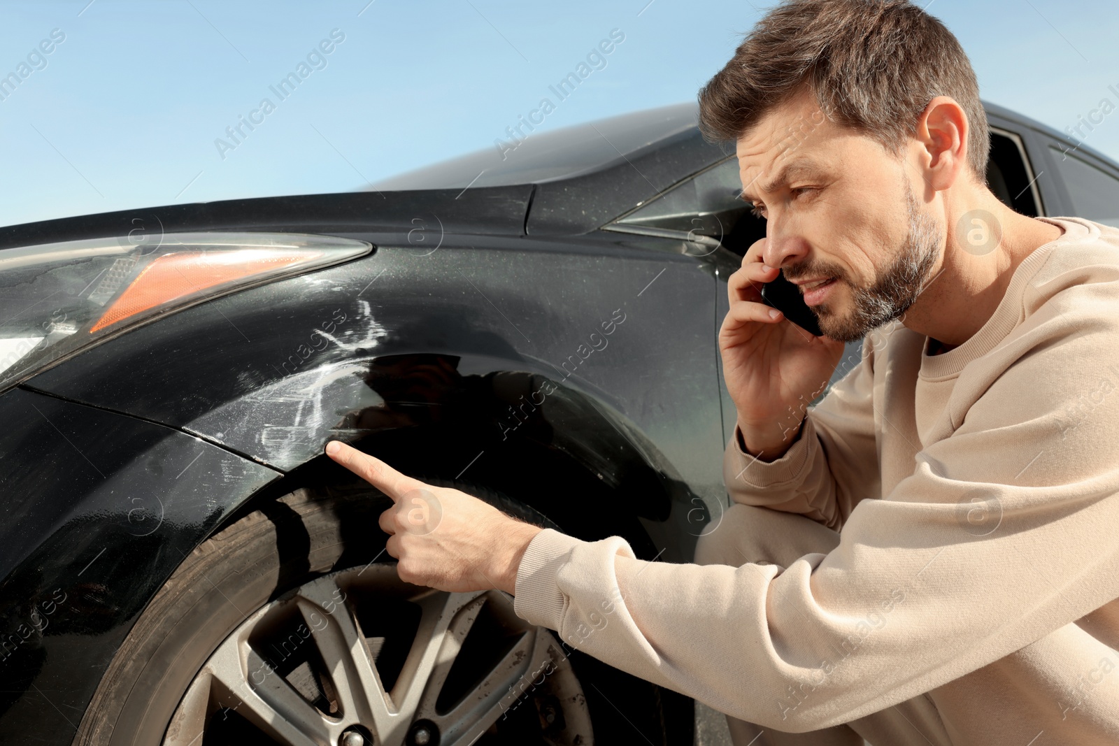 Photo of Man talking on phone near car with scratch outdoors