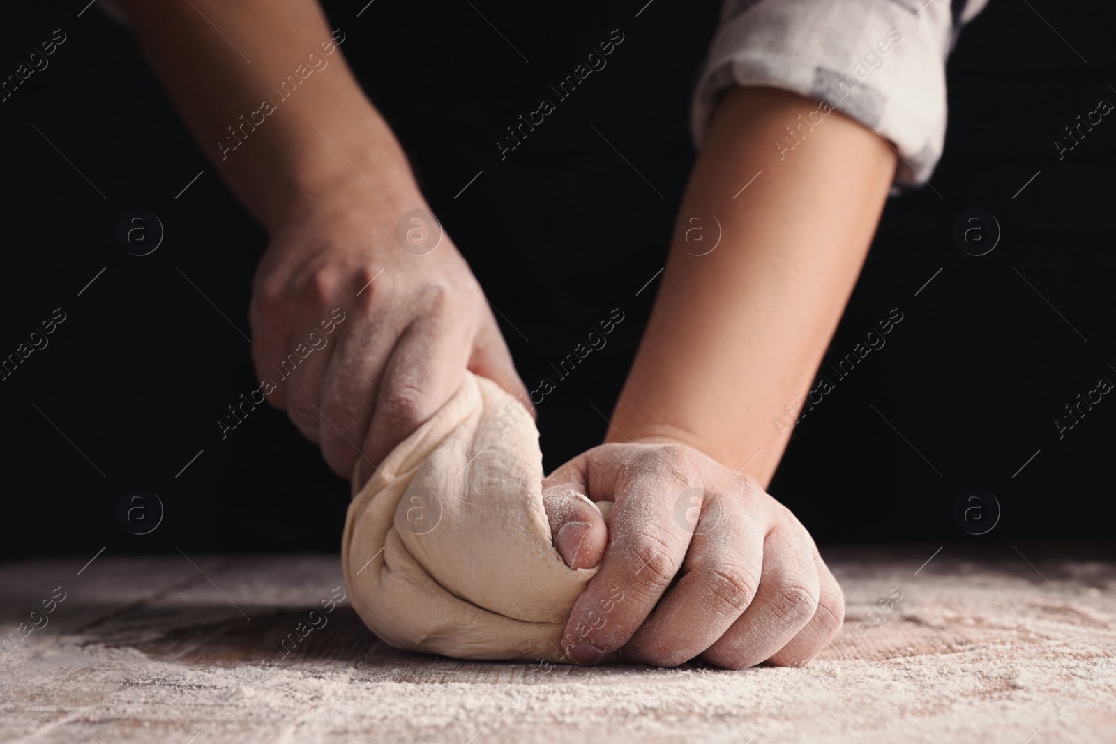 Photo of Man kneading dough at wooden table on dark background, closeup