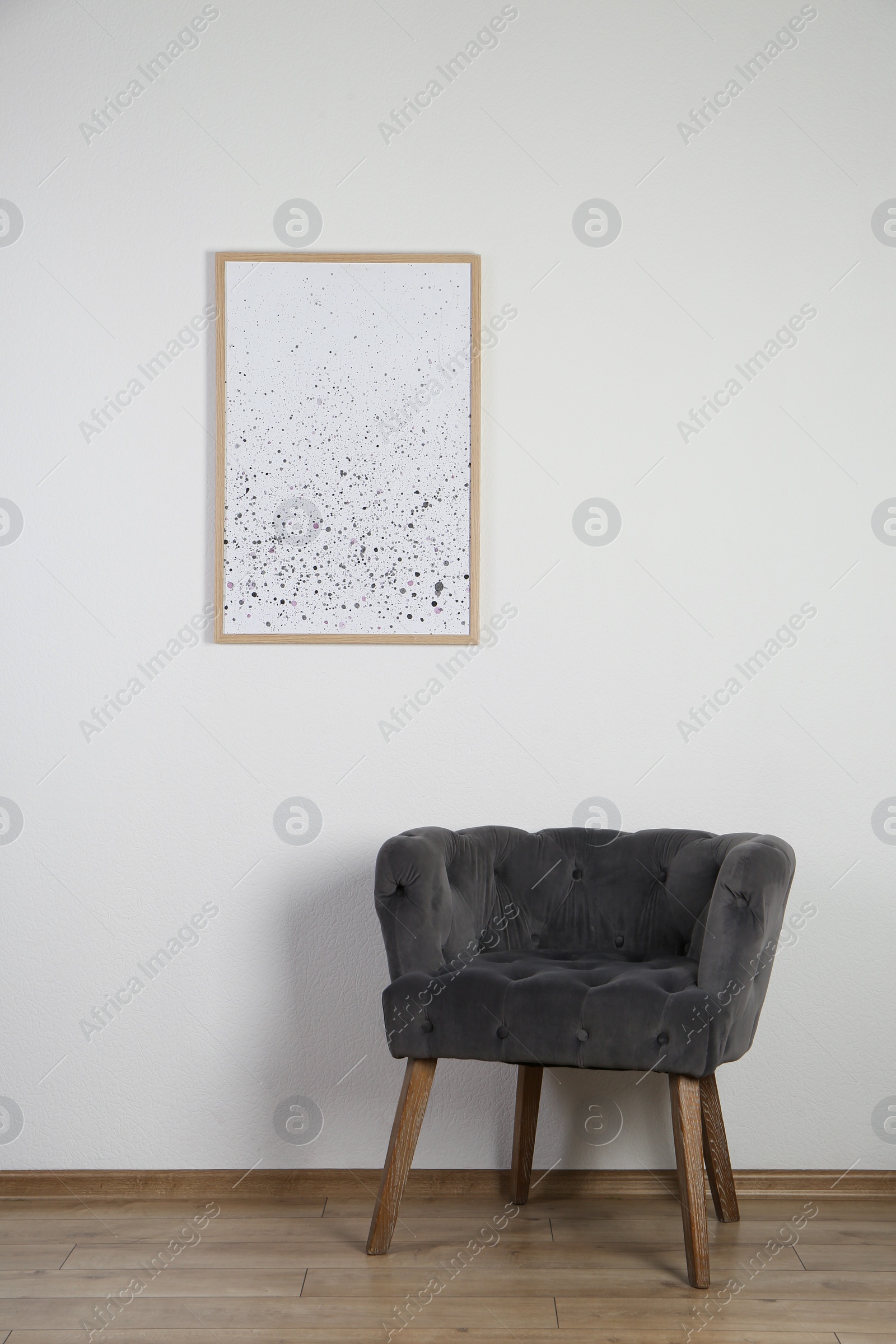 Photo of Comfortable armchair, cushion and picture frame on wall indoors. Interior element