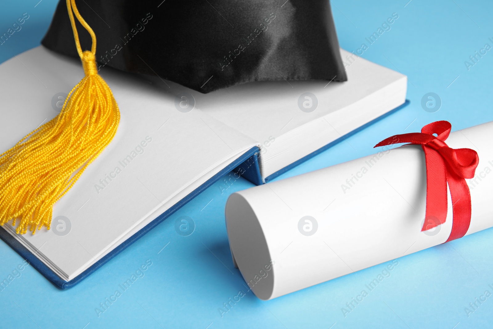 Photo of Graduation hat, open book and student's diploma on light blue background, closeup