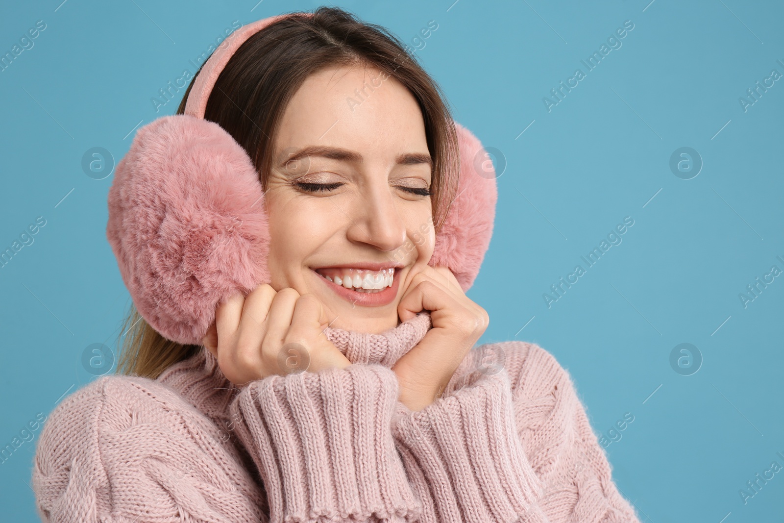 Photo of Happy woman wearing warm earmuffs on light blue background